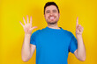 © Roquillo - young handsome caucasian man wearing blue t-shirt against yellow background showing and pointing up with fingers number six while smiling confident and happy.