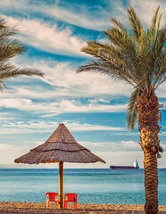 Tropical exotic beach with two resting chairs and rustic sunshade or umbrella, yellow sand and Red sea waters, perfect relax in holiday luxury destination