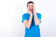 © Roquillo - Doleful desperate crying young handsome caucasian man wearing blue t-shirt against white background, looks stressfully, frowns face, feels lonely and anxious