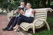 © sofiko14 - Happy mature couple using digital tablet while sitting in embrace on wooden bench. Relaxation at green park. Concept of modern technology.