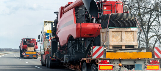 Wall Mural - Many heavy industrial truck with semi trailer platform transport disassembled combine harvester machine on public highway road on sunset or sunrise day. Agricultural equipment transportation service