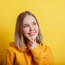 Happy Smiling Young Woman Think Thought. Portrait Of Emotional Teenage Girl Thinking About Idea Or Positive Question On Color Yellow Background. Square
