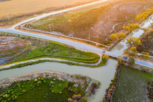 Aerial View Of A Bridge Crossing An Inlet Channel Through An Arid Landscape At Sunset