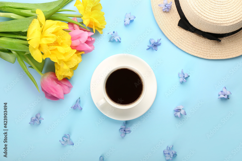 Cup of coffee with flowers and hat on color background