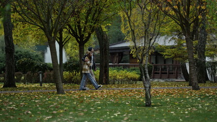 Wide shot of young walking couple going along scenic wood path in early autumn. 