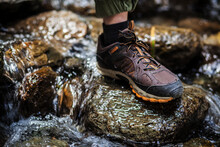 A Foot In A Brown Trekking Boot Stands On A Wet Rock In A Mountain River