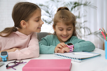 Girls with stylish smart watches at table indoors