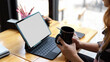 © bongkarn - Female holding coffee cup while working on her project with blank screen tablet