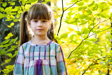 Wall Mural - Portrait of happy pretty child girl having fun in autumn forest. Positive female kid enjoying warm day in fall park.