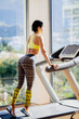 © shevtsovy - young attractive woman running on treadmill in sport gym. Attractive sporty girl in sportswear jogging on running track morning routine.