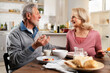© JustLife - Senior couple eating breakfast together in the kitchen. Husband and wife enjoying in the morning.