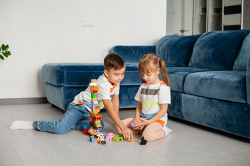 Two young children boy and girl sit on the wooden floor of the house playing educational games