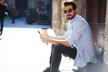 Wall Mural - Young bearded man drinking coffee while resting in town