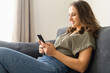 © Vadim Pastuh - Satisfied young woman with smartphone on the couch rests at home, leaned back in relaxed pose, scrolling news, chatting in social media with friends, messaging online, chatting in date app. Side view
