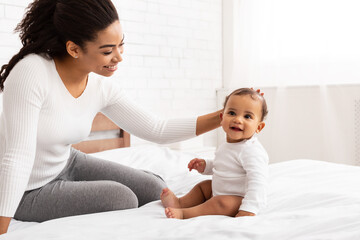 Wall Mural - African American Mom Stroking Baby Toddler Sitting On Bed Indoor