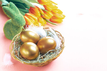 Wall Mural - Easter eggs Golden color in basket with spring tulips, white feathers on pastel pink background in Happy Easter decoration. Festive decoration.