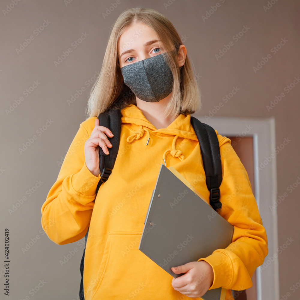 Schoolgirl in mask with backpack and notepad. Young woman student in protective medical mask. Portrait of blonde female student Girl at university interior during coronavirus covid 19 lockdow. Square