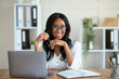 Portrait of cheerful black business lady sitting at her desk with laptop, smiling at camera in office