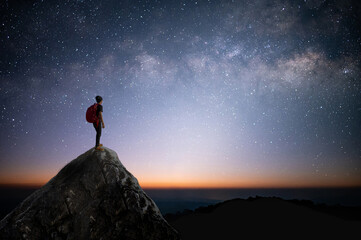 Silhouette of young traveler and backpacker standing on the rock watched the star and milky way. He enjoyed traveling and was successful when he reached the summit.