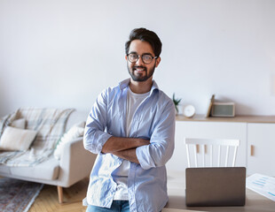 Wall Mural - Modern Entrepreneur. Cheerful Young Eastern Man Standing Near Desk At Home Office