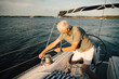 © Maskot - Senior man tying rope on cleat while kneeling in boat during sunny day