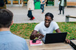© Maskot - Young male student laughing while sitting with friend in campus