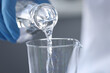 Scientist chemist in gloves pouring water from flask into glass closeup