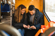© Maskot - Heterosexual couple using smart phone while sitting in tram during pandemic