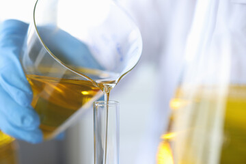 Scientist chemist pouring oil from flask into glass closeup