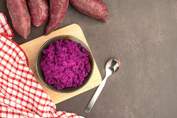 Sticker - Purple yams pile and mashed purple sweet potatoes on a bowl placed on a cutting wooden board on a dark brown background. Space for text. Vintage background.  Healthy fruits concept