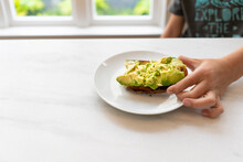 Young Child Eating Green Avocado Toast For Breakfast At The Kitchen Counter