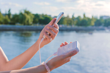 Wall Mural - Power Bank and a smartphone in the hands of a girl. Against the background of the embankment.