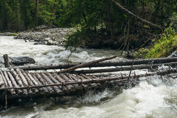 Fast turbulent river with broken bridge in water. Scenic mountain landscape with log bridge across river. Beautiful scenery with wooden bridge over mountain creek. Powerful rapids in mountain river.