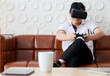 © Bangkok Click Studio - Asian old middle aged black hair male senior grandfather wears white shirt black pants sit on brown leather sofa play virtual reality game alone from 3d vr goggles headset hold two hands up in air