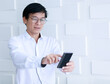 © Bangkok Click Studio - Close up shot hand and index finger of Asian old middle aged happy male businessman wears white long sleeve shirt and eyeglasses stand in blurred background pointing at small black screen smartphone