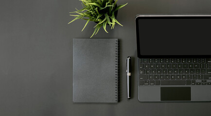 Mockup top view of tablet with keyboard, notebook, pen and houseplant on black background.