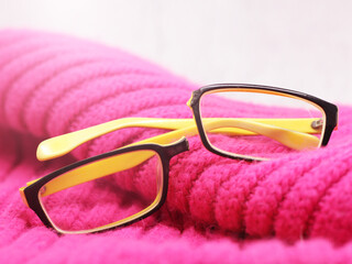 Broken yellow-rimmed glasses on a pink knit scarf