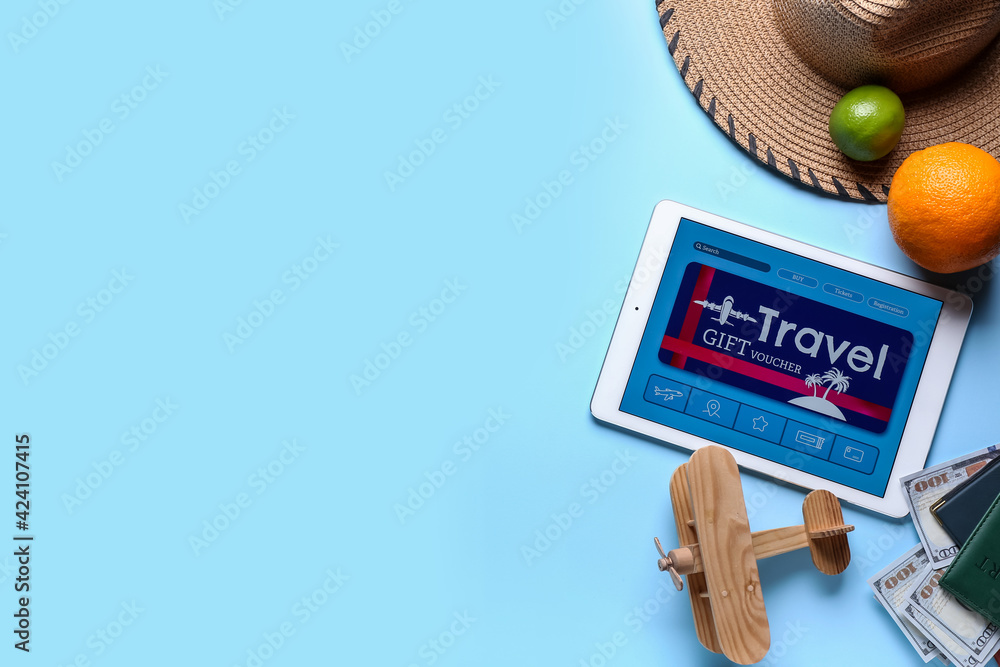 Tablet computer with gift voucher and travel accessories on color background