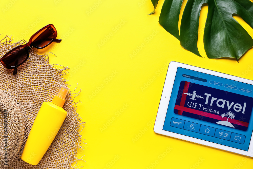 Tablet computer with gift voucher and travel accessories on color background