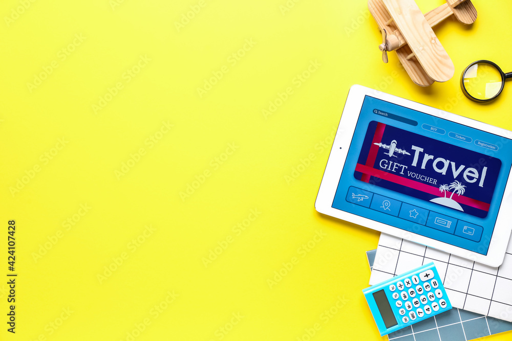 Tablet computer with gift voucher and travel accessories on color background