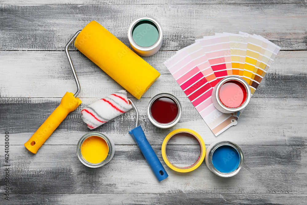 Cans of paints, rollers and palette samples on light wooden background