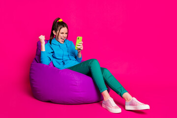 Sticker - Full length photo of lucky young lady wear blue sweater relaxing violet beanbag looking modern device isolated pink color background