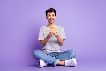 Sticker - Photo of positive guy hold cellphone look empty space wear black t-shirt jeans footwear isolated violet background