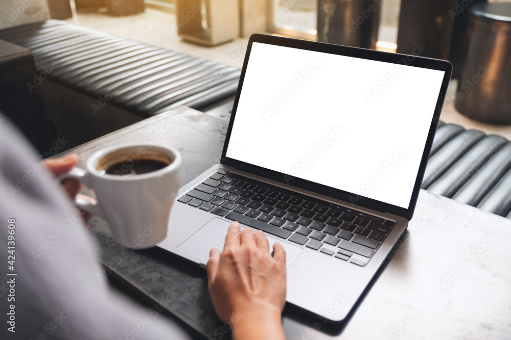 Mockup image of a woman using and touching on laptop touchpad with blank white desktop screen while drinking coffee - obrazy, fototapety, plakaty 