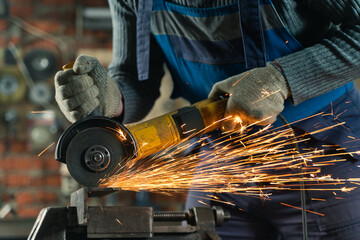 Locksmith in special clothes and goggles works in production. Metal processing with angle grinder. Sparks in metalworking