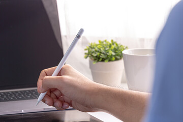 Man with a pen writing on a tablet working and laptop on home office workspace