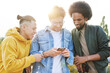 © gpointstudio - Three young smiling men standing and scrolling mobile phone