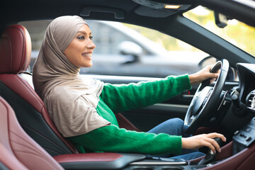 Wall Mural - Smiling muslim woman test driving new car in urban city