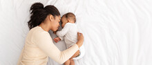 African Mother Hugging Sleeping Baby Lying In Bed Indoor, High-Angle