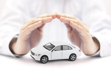 Car Insurance Concept With White Car Toy Covered By Hands